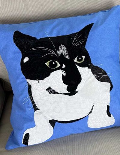 This fabric pet portrait pillow shows off the cat's white whiskers and eyebrows. The black and white cat is on a light blue background.