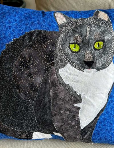 Fabric pet portrait pillow of grey cat with white bib on bright blue background