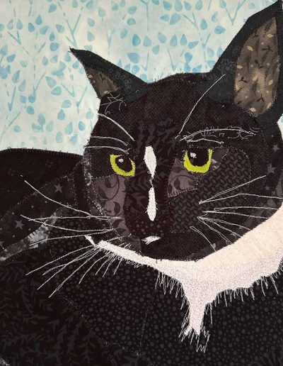 This canvas mounted fabric pet portrait of a black cat shows off his white whiskers and eyebrows. The white fur at his neck is accentuated by white thread painting.